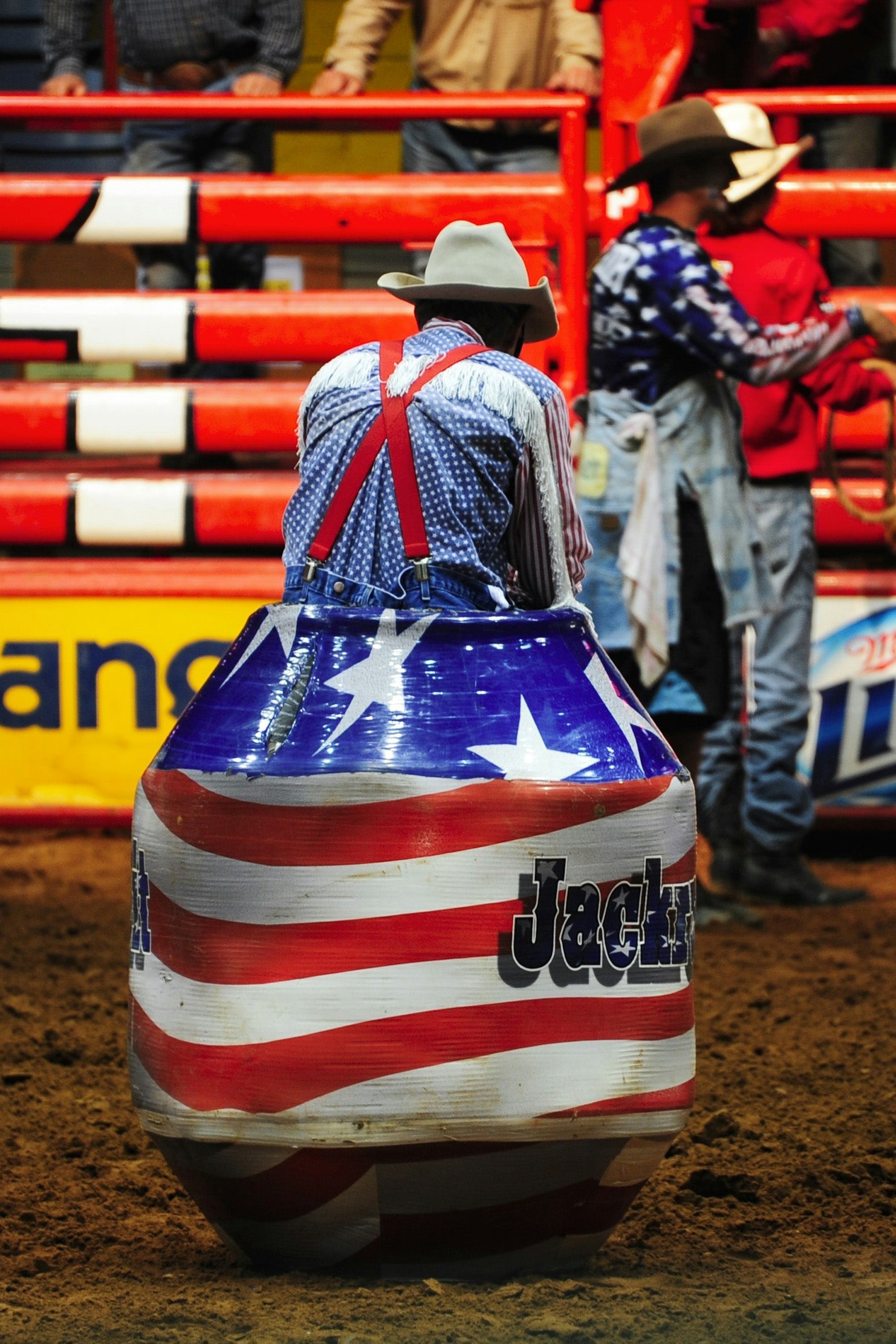 rodeo clown seated on a barrel in an arena