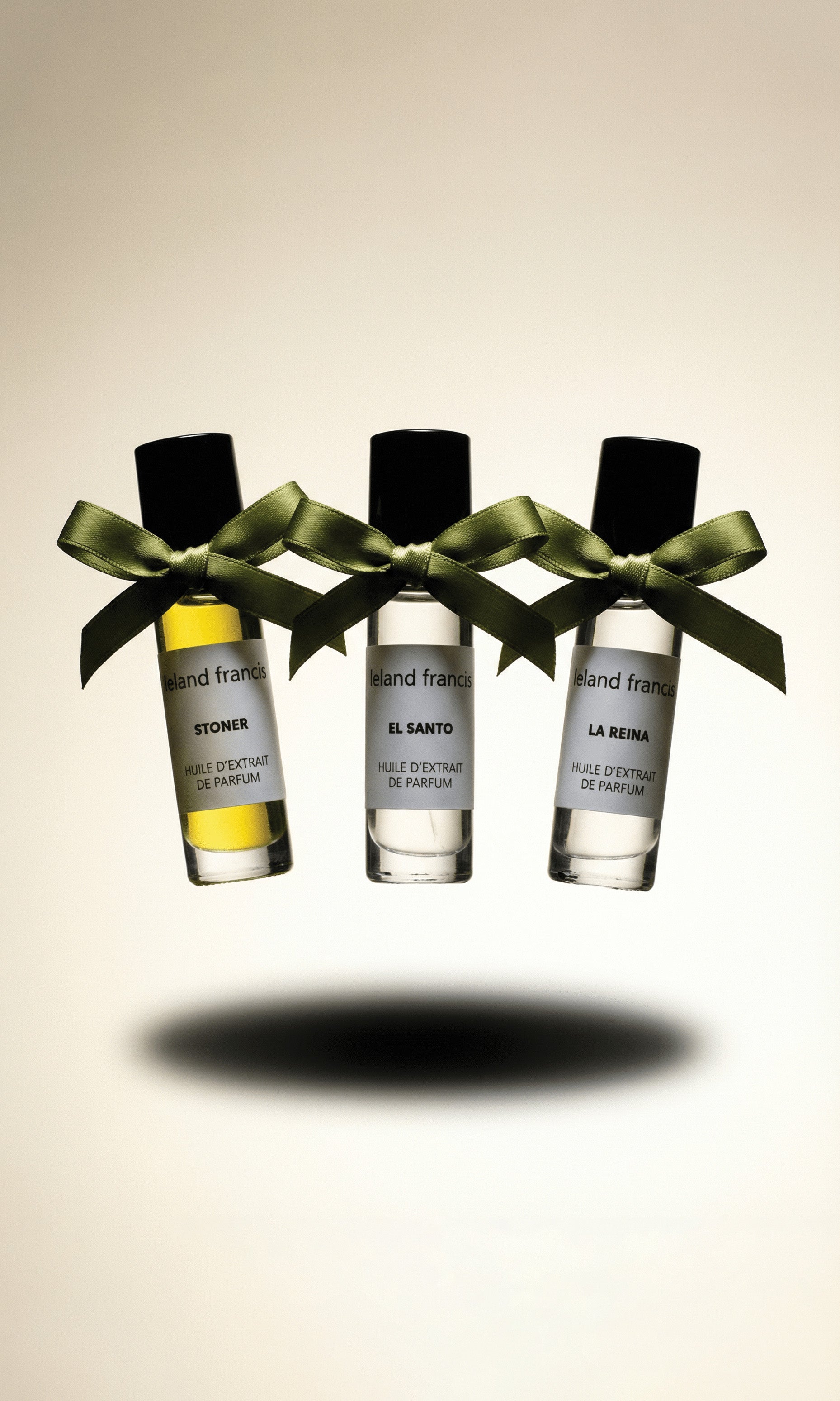 Three perfume bottles with green ribbons on a beige background