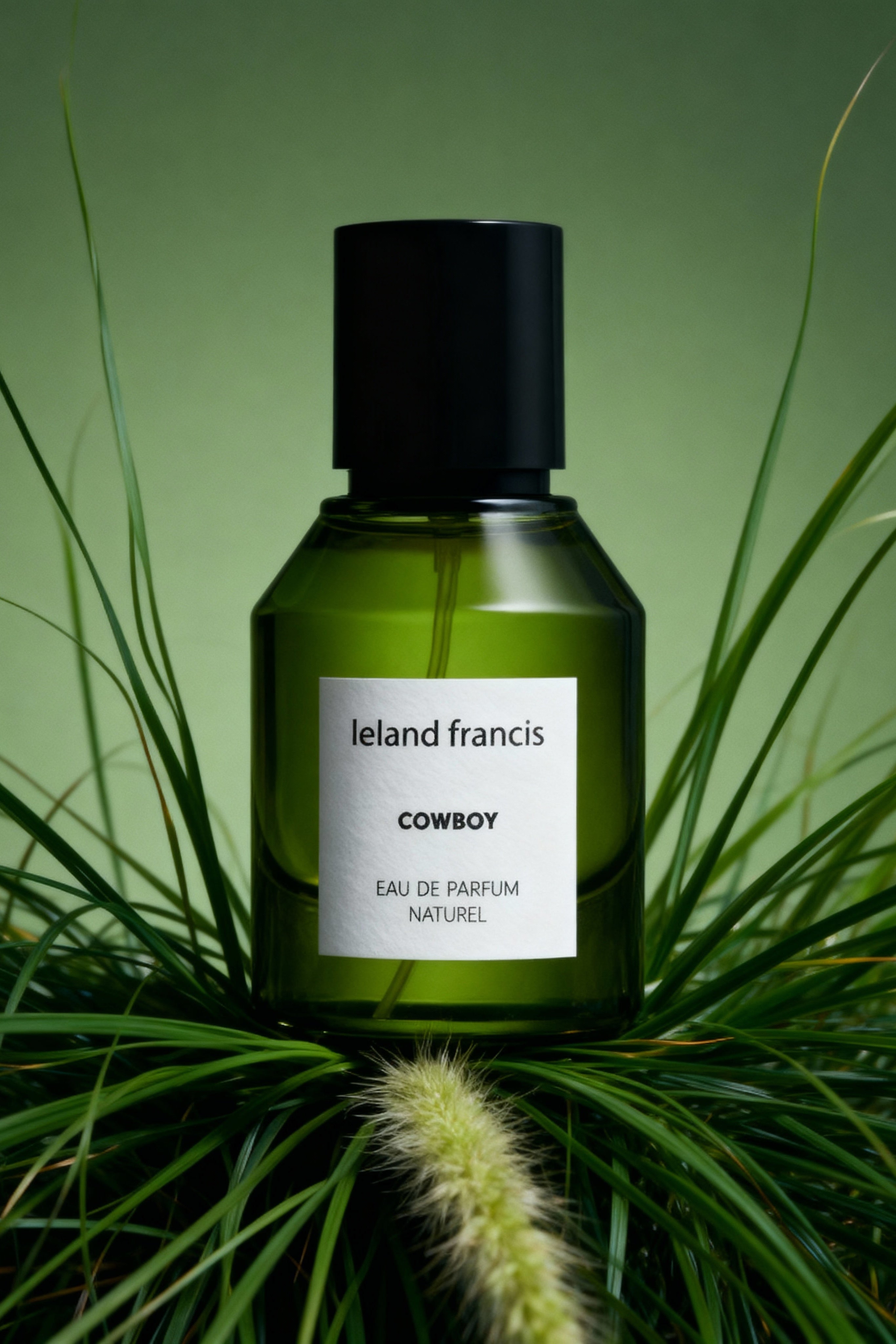 Green perfume bottle labeled 'Ieland Francis Cowboy' on a green background with grass.