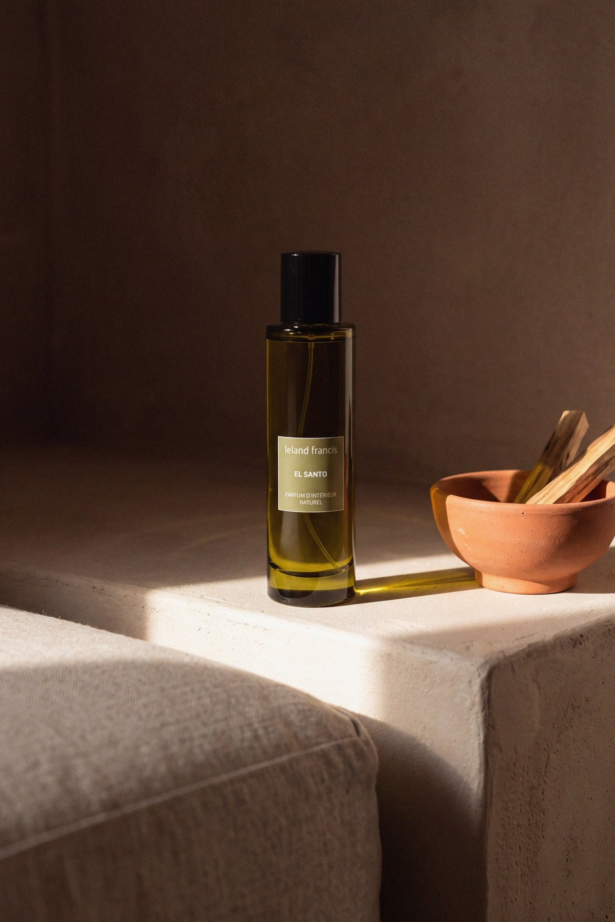 El Santo Room Spray on a plaster ledge beside a terracotta bowl of palo santo, afternoon light