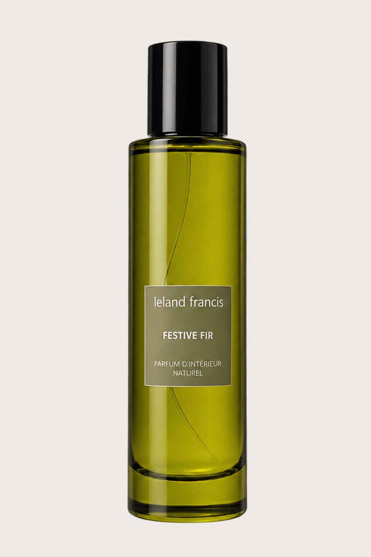 A tall, cylindrical glass bottle of Leland Francis Festive Fir natural fragrance, filled with an olive-green liquid and topped with a black cap, set against a solid light gray background.