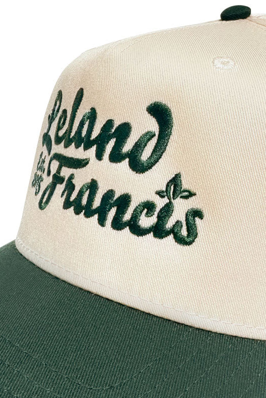 Beige and green cap with 'Leland Francis' embroidery on a white background