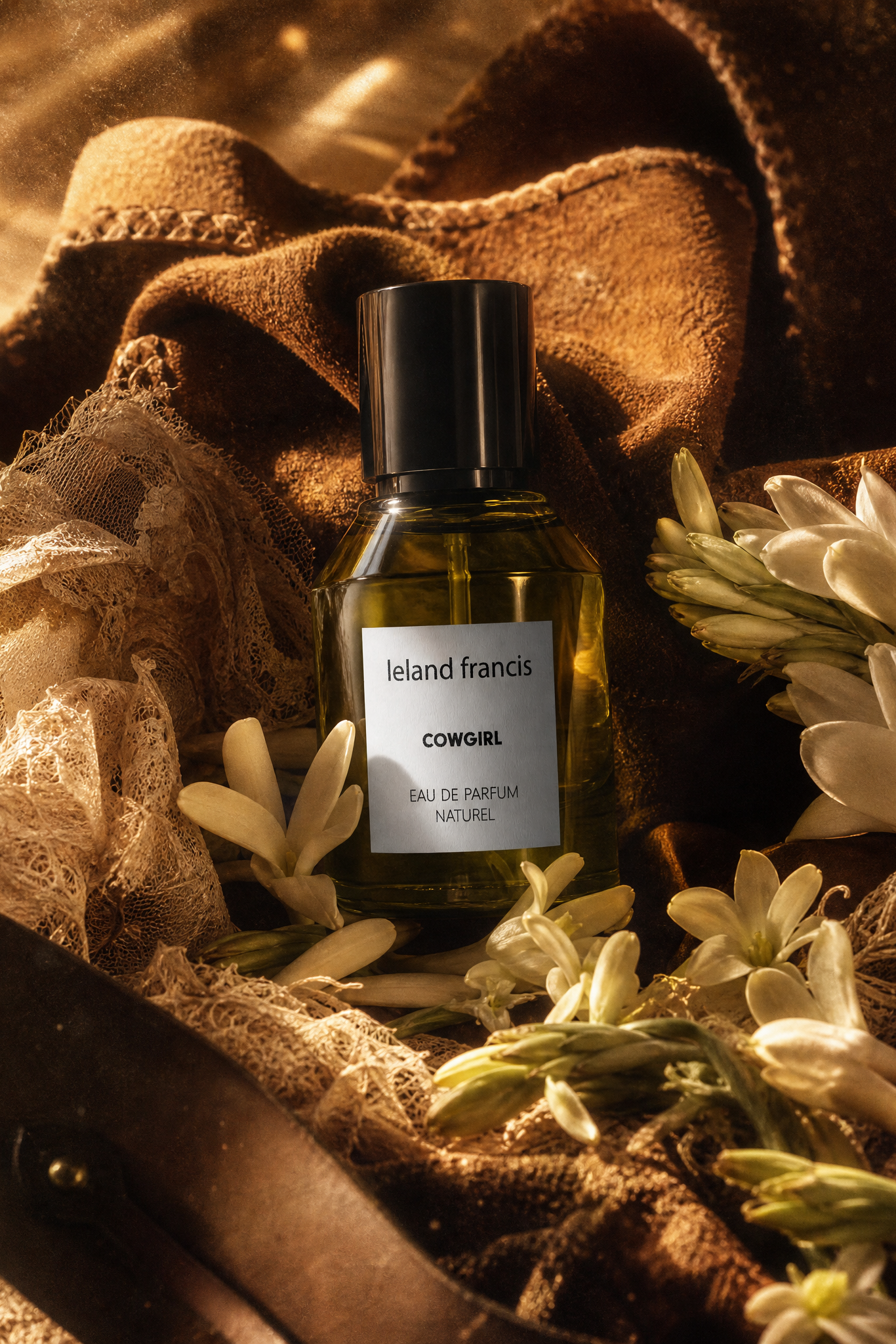 Perfume bottle labeled 'Ieland Francis' surrounded by flowers and fabric in a warm-toned setting