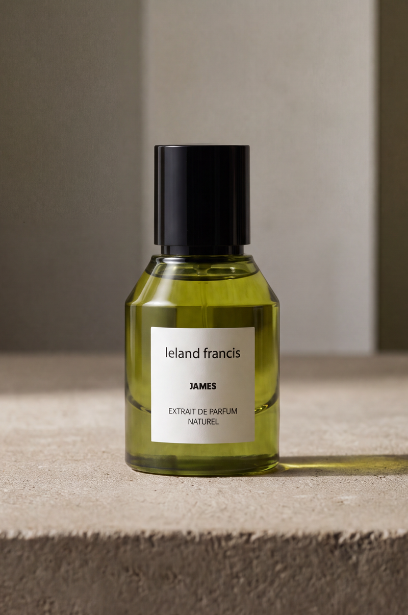 A bottle of Leland Francis James natural fragrance with a black cap and white label, set on a textured concrete ledge against a neutral beige background.