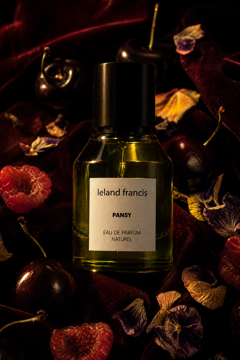 Ieland Francis Pansy perfume bottle surrounded by flowers and fruits on a dark background